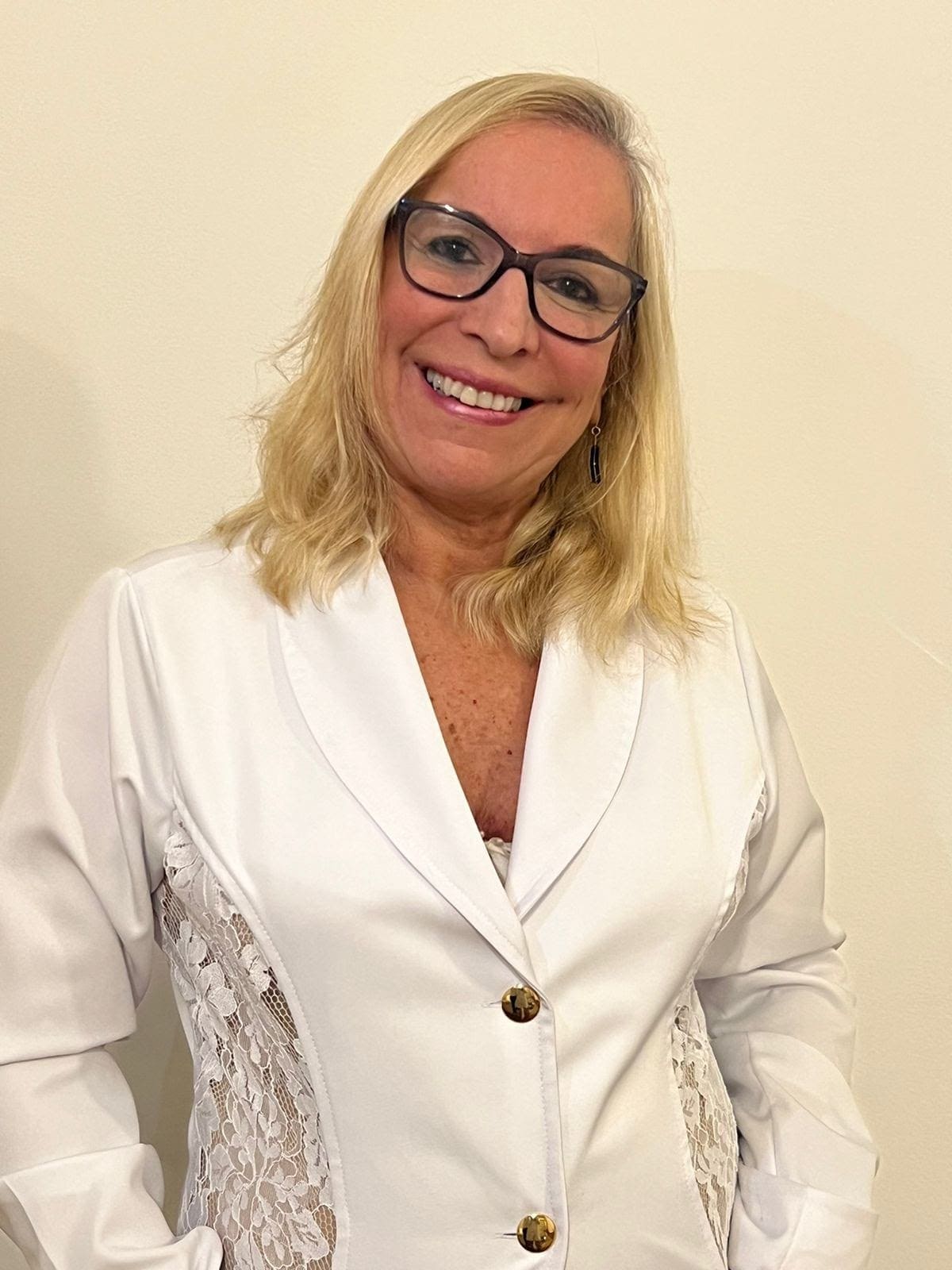 Retrato vertical da Dra. Clotilde de Souza em seu consultório odontológico, ambiente sofisticado com tons claros e detalhes em dourado, iluminação ambiente elegante, equipamentos odontológicos modernos ao fundo desfocados, composição 3/4, fotografia profissional com bokeh suave, paleta bege-dourado-branco